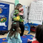 A teacher using an alligator puppet for an interactive circle time lesson in the GMCC classroom