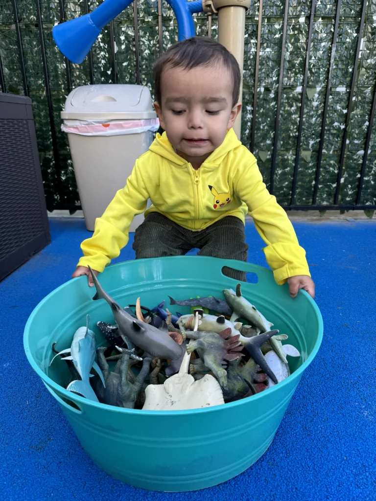 A toddler exploring a bucket of sea animal toy figures during sensory play at GMCC