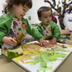 Two toddlers working together on a collaborative canvas painting project at GMCC childcare