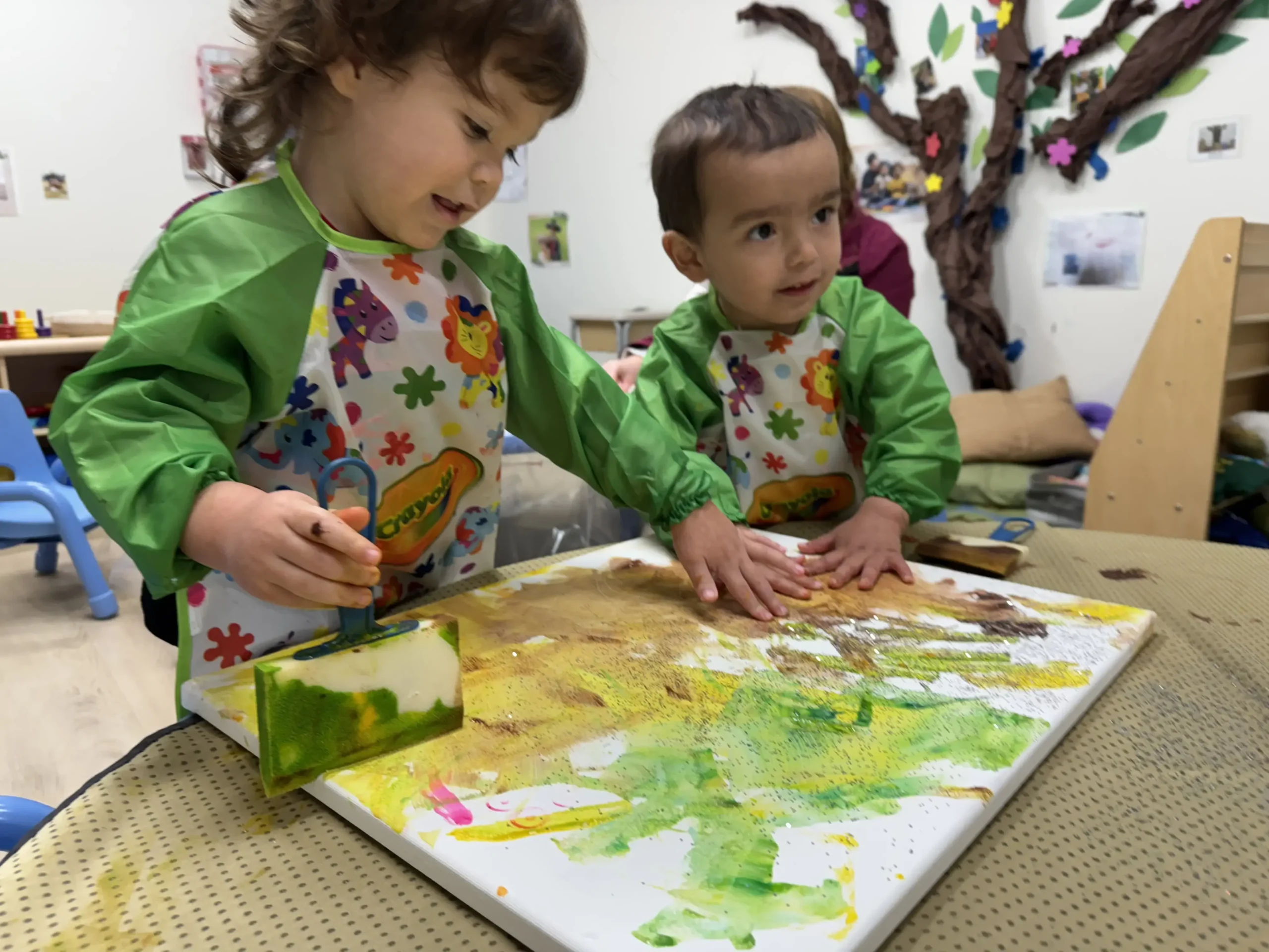 Two toddlers working together on a collaborative canvas painting project at GMCC childcare