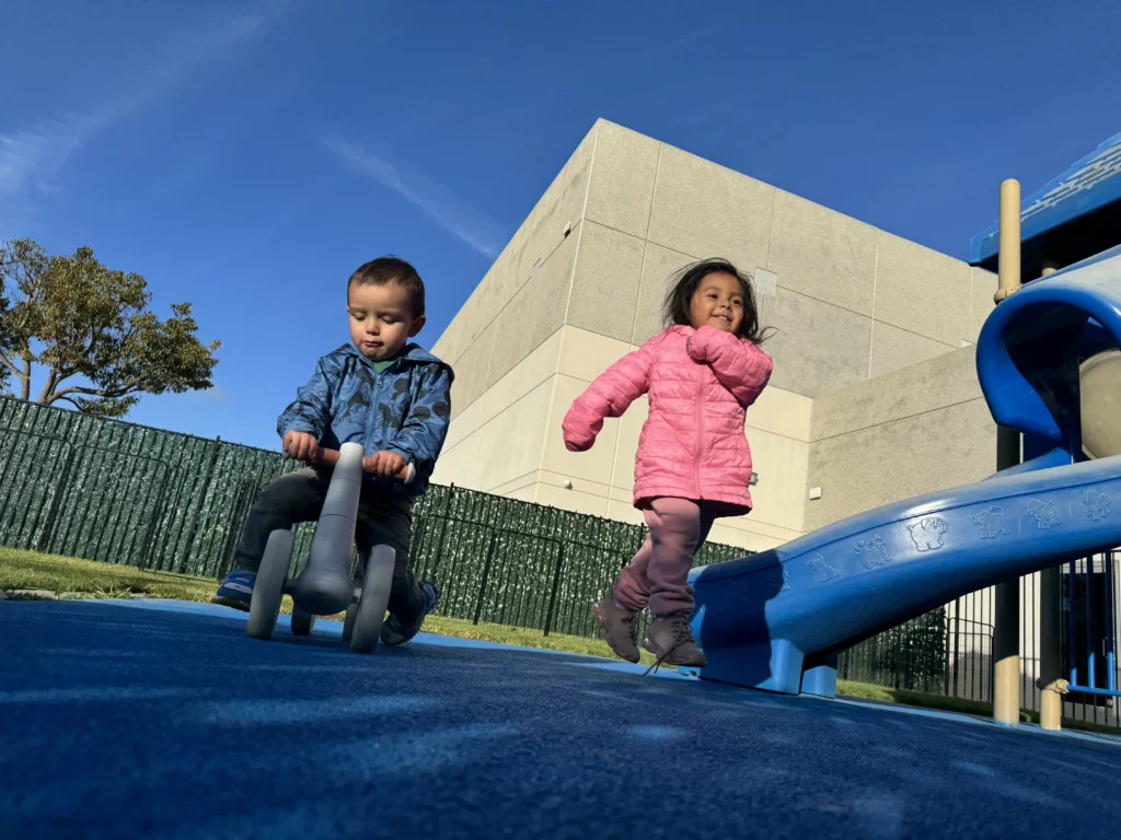 Toddlers enjoying outdoor play with ride-on toys near the playground at GMCC childcare