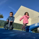 Toddlers enjoying outdoor play with ride-on toys near the playground at GMCC childcare