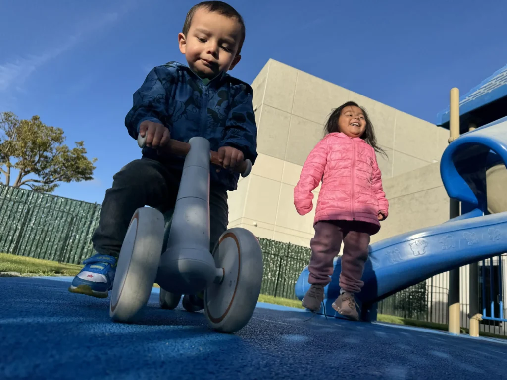 A toddler riding a balance bike while playing at the GMCC outdoor playground area