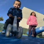 A toddler riding a balance bike while playing at the GMCC outdoor playground area